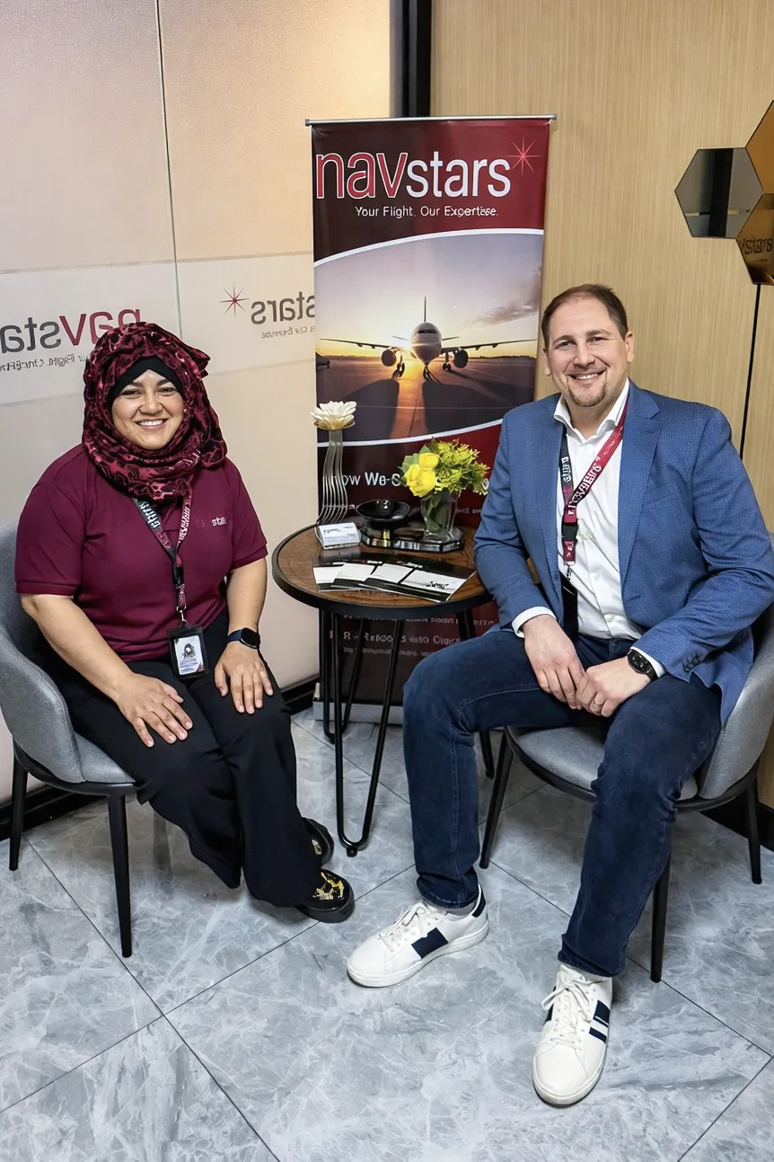 NavStars Managing Director Andrea Magnano and Business Operations Director Dana Viray seated together in the NavStars office lounge, with a NavStars roll-up banner visible between them.